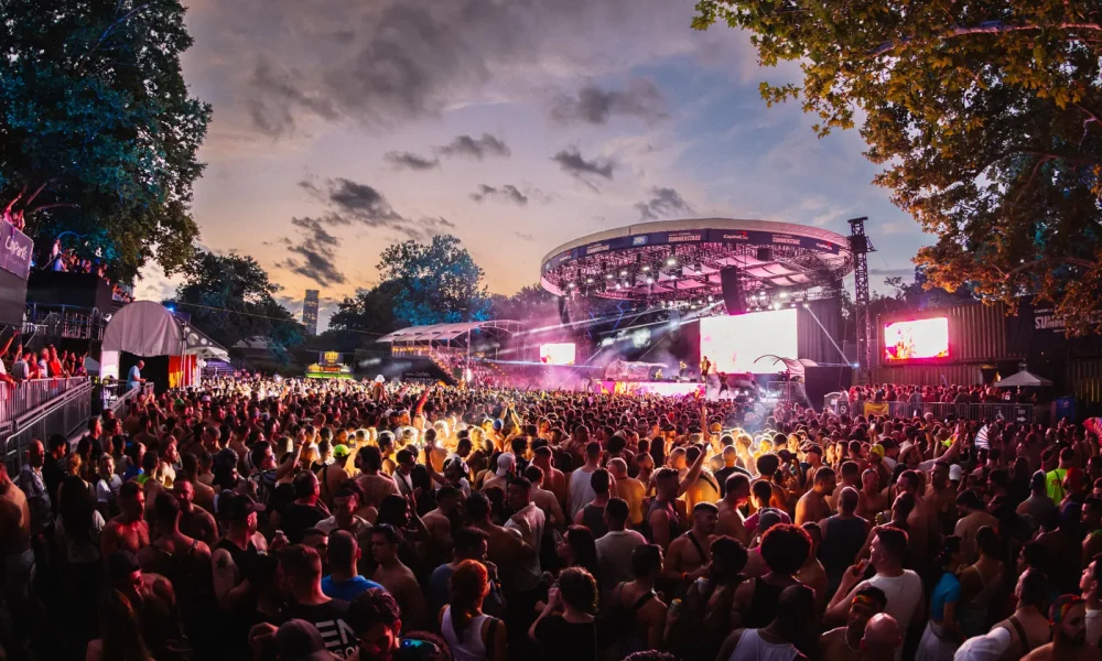 Dreamland Pride crowd and illuminated SummerStage surrounded by trees in Central Park.